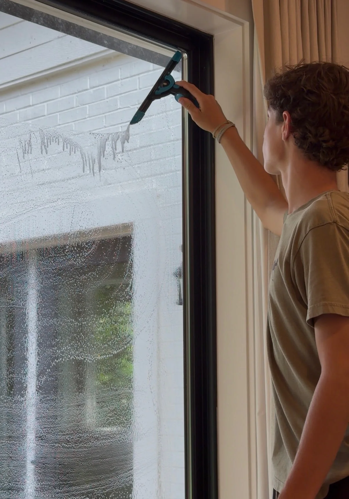 Brooks Safley cleaning an interior window by hand with a squeegee.